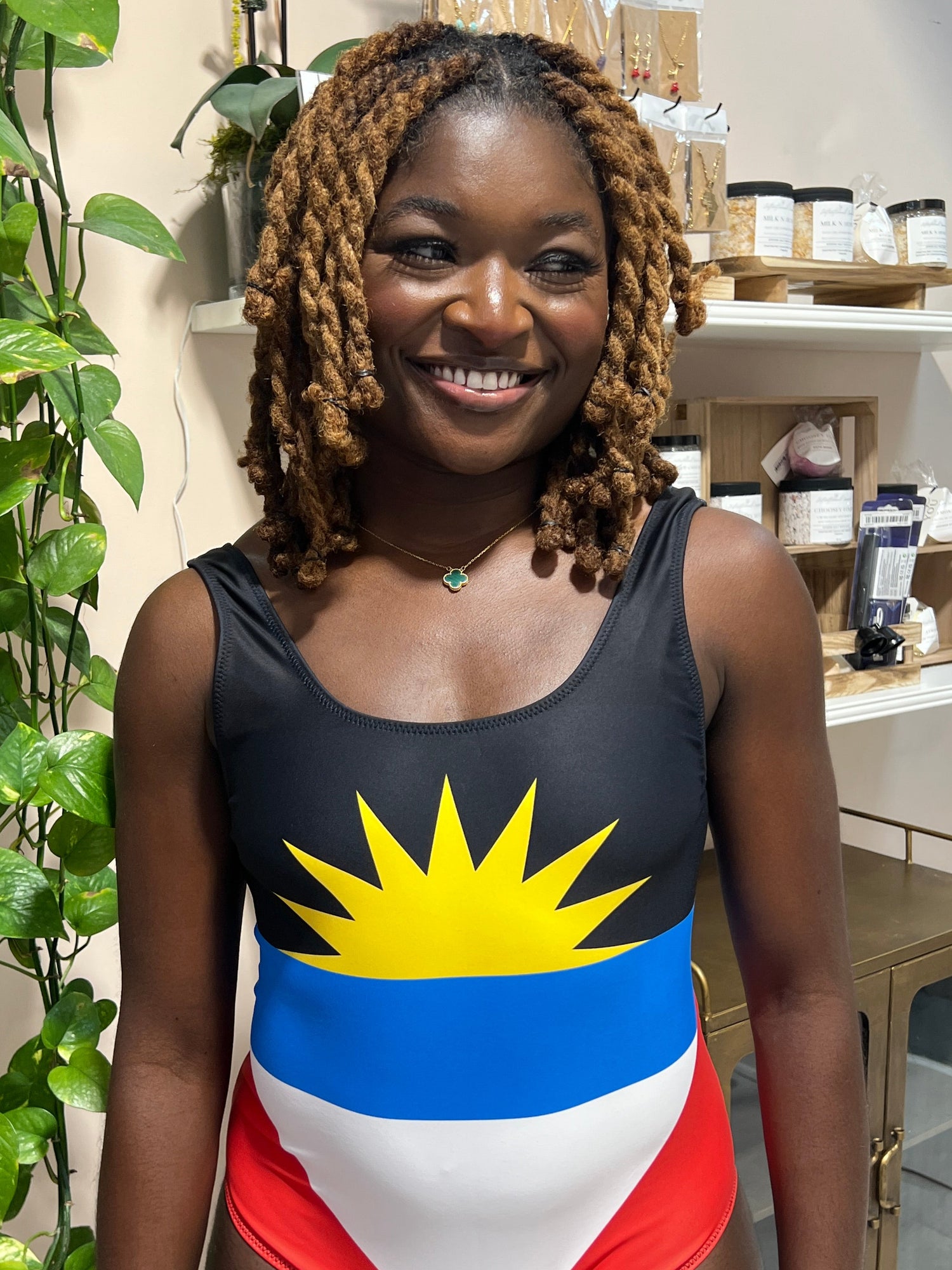 woman wearing a Antigua and barbuda flag swimsuit, standing indoors with plants